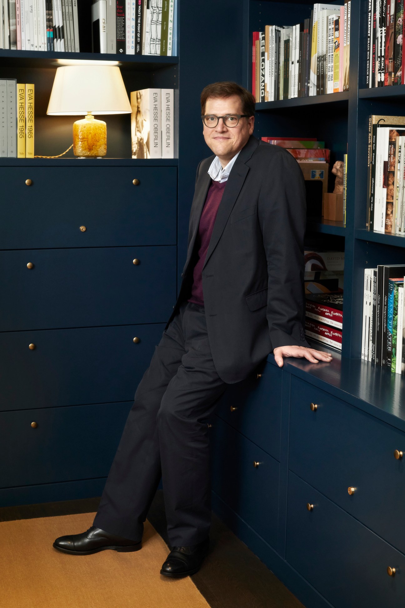 James Koch in dark suit and glasses standing in front of blue built-in bookshelves in office setting