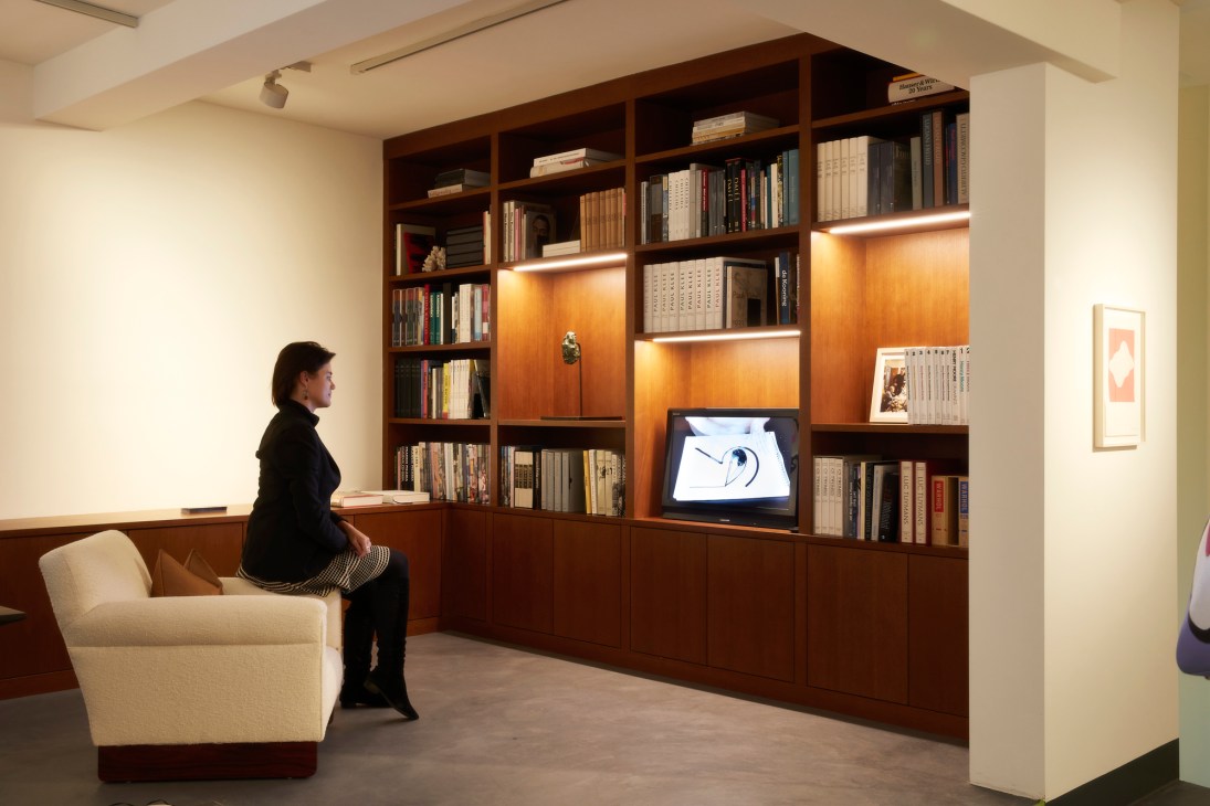 Woman sitting in modern lounge area with built-in wooden bookshelves and integrated television screen