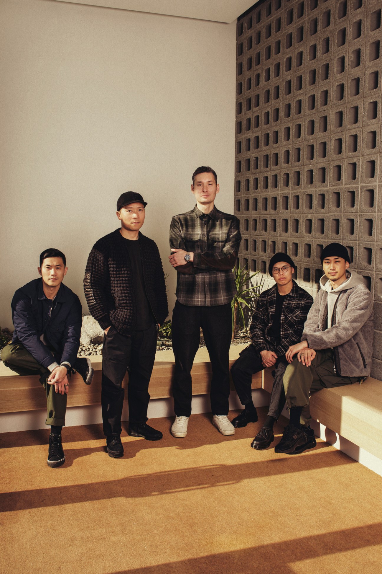 Five men in casual menswear posing together in modern interior with concrete block wall and wooden flooring