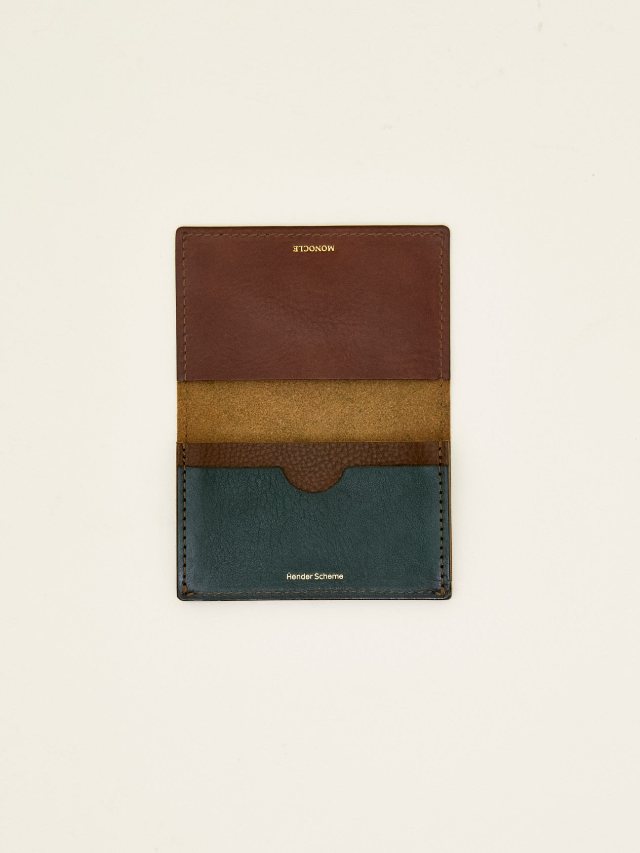 Multi-colored leather card case with brown, olive and teal panels displayed flat against beige background
