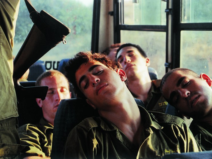 Four young men in military uniforms sleeping on a bus