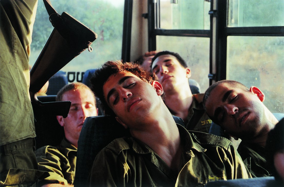 Four young men in military uniforms sleeping on a bus