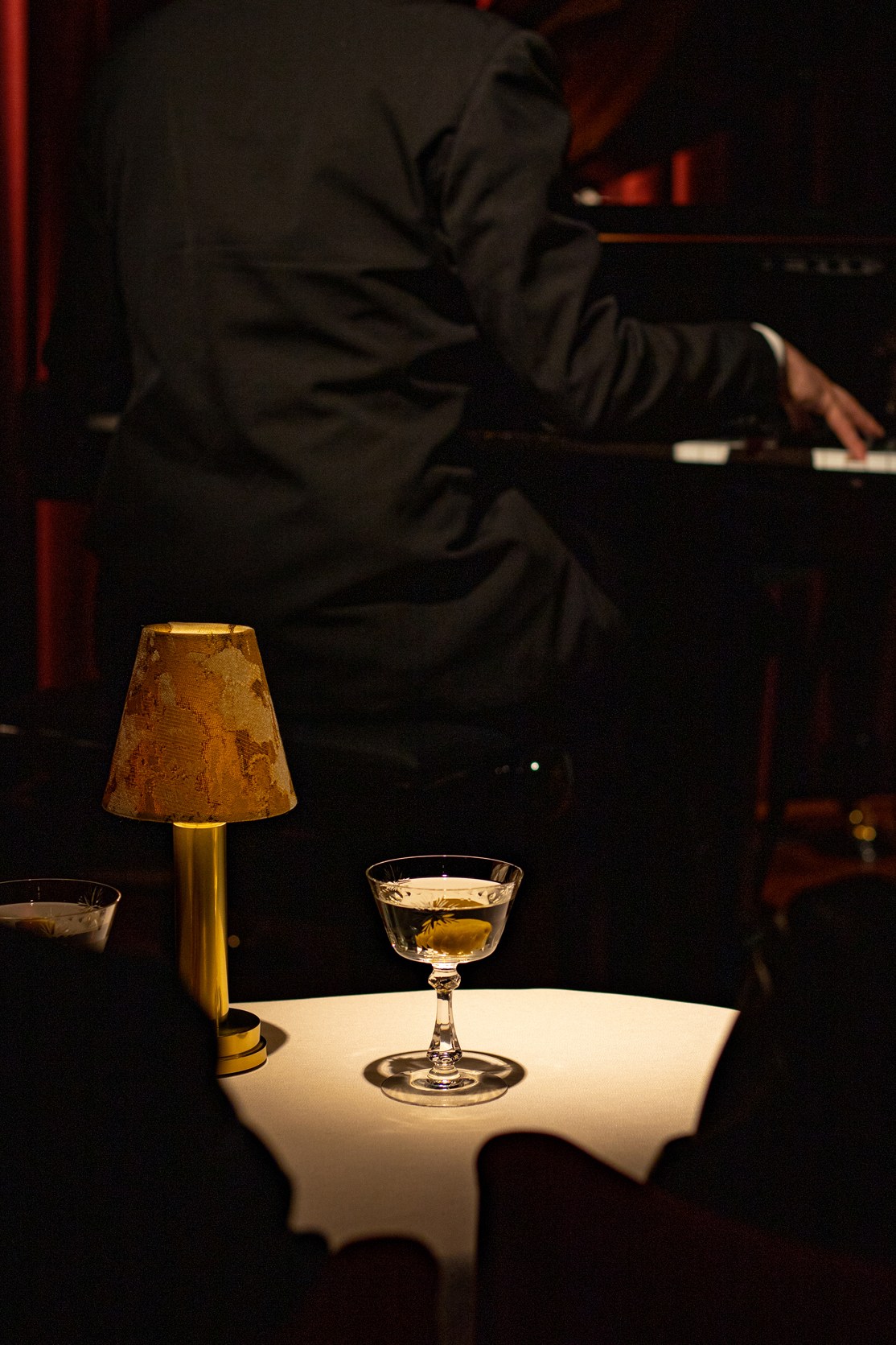 A martini glass and brass table lamp on a white table at Carlyle & Co bar in Hong Kong.