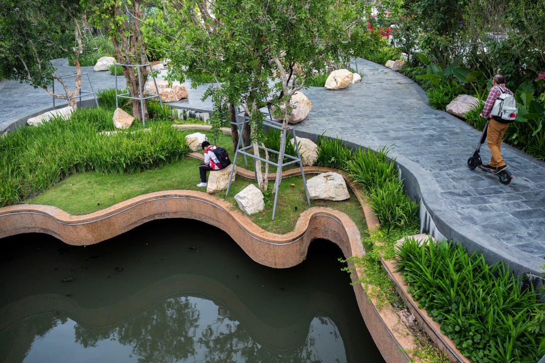 Curved pedestrian bridge over Chong Nonsi Canal with visitors enjoying landscaped park areas and walkways