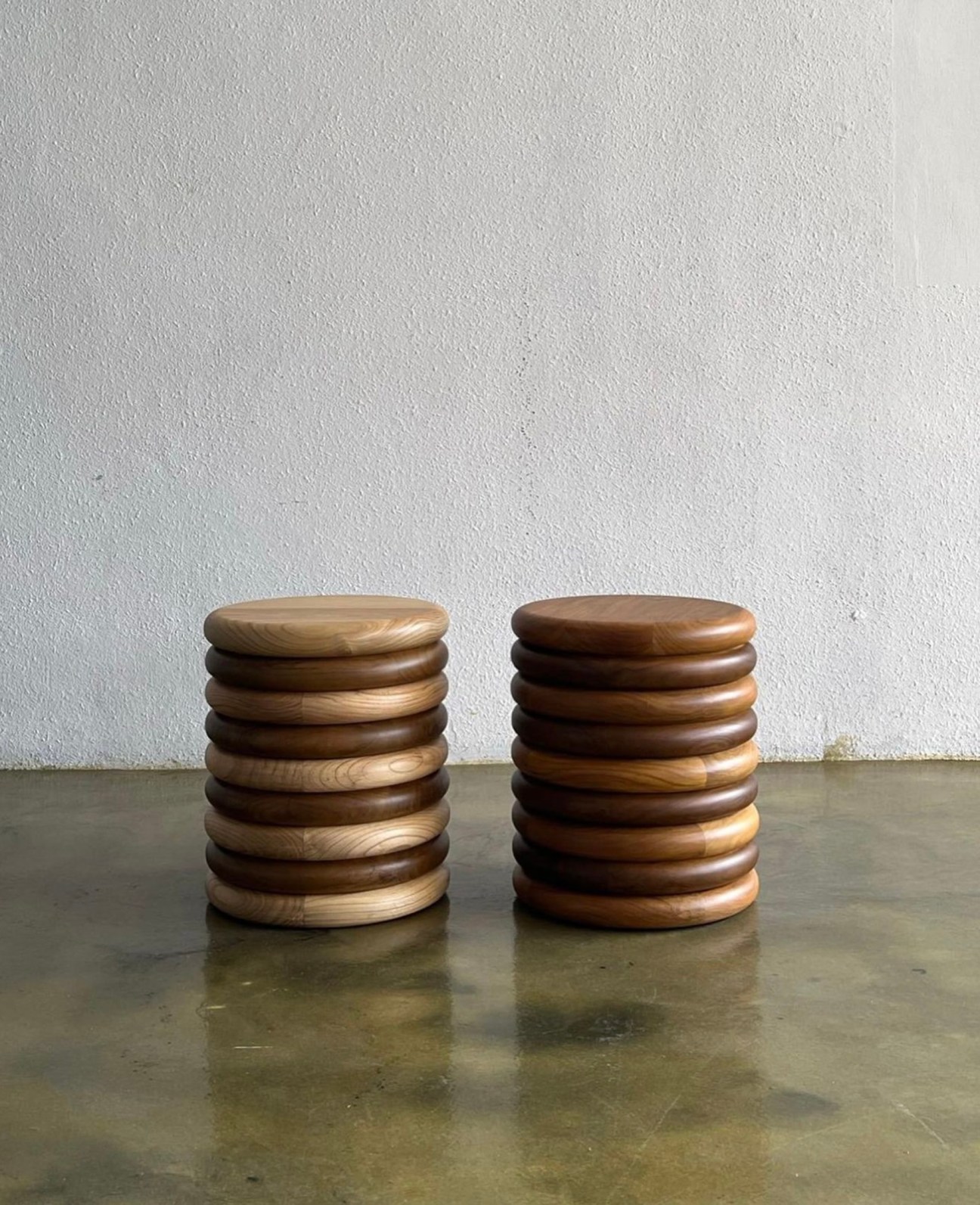 Two wooden Hilu stools with stacked circular disc design by Studio Kallang on polished concrete floor
