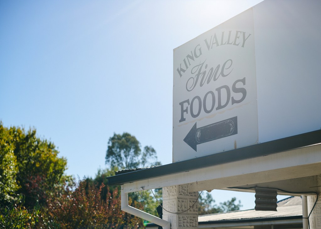 White directional sign for King Valley Fine Foods with black arrow pointing left mounted on building exterior