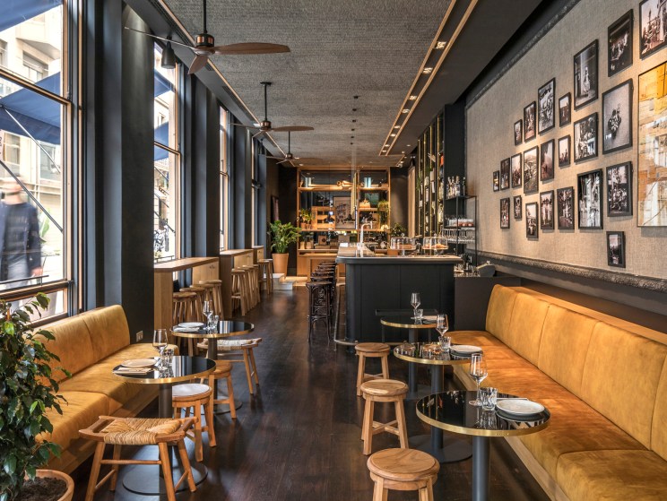 Interior of Casa Sagnier hotel bar with orange banquette seating, wooden stools, and framed photographs on walls