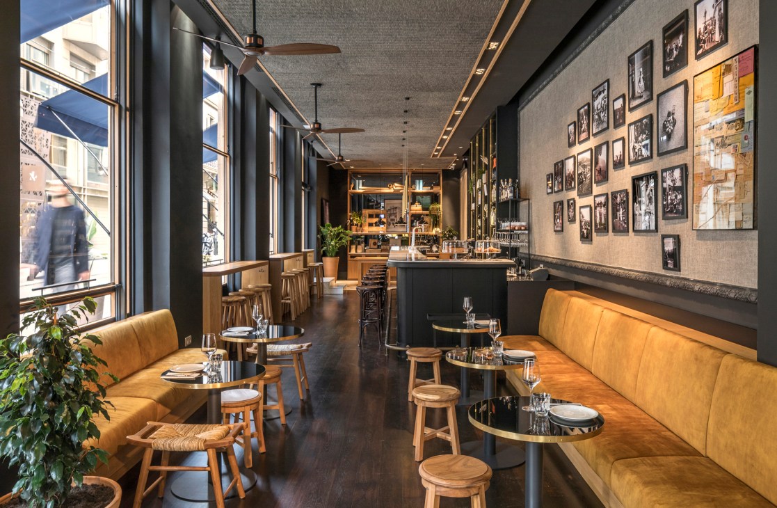 Interior of Casa Sagnier hotel bar with orange banquette seating, wooden stools, and framed photographs on walls