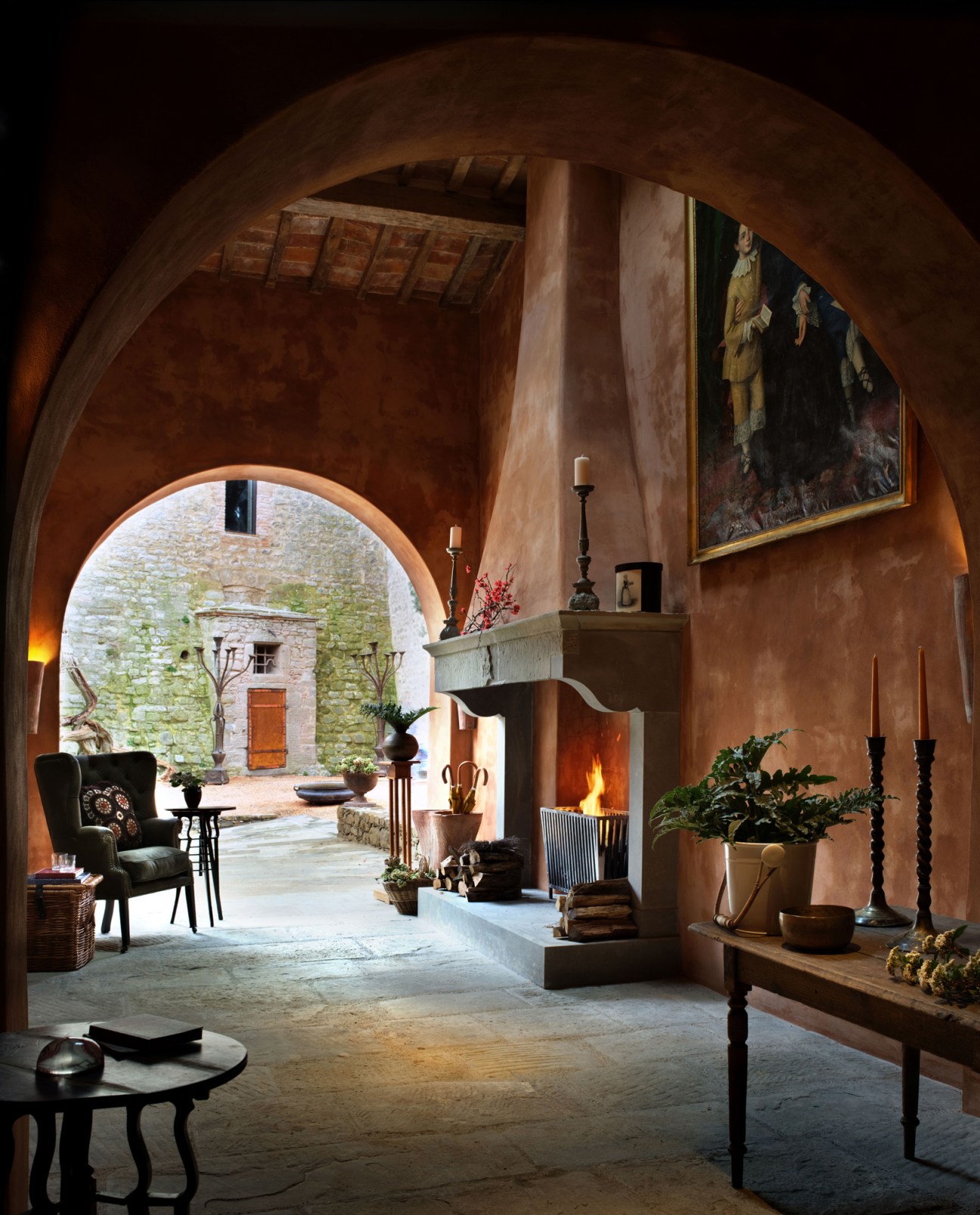 Arched stone interior with fireplace, wooden furniture, candlesticks and view to courtyard beyond