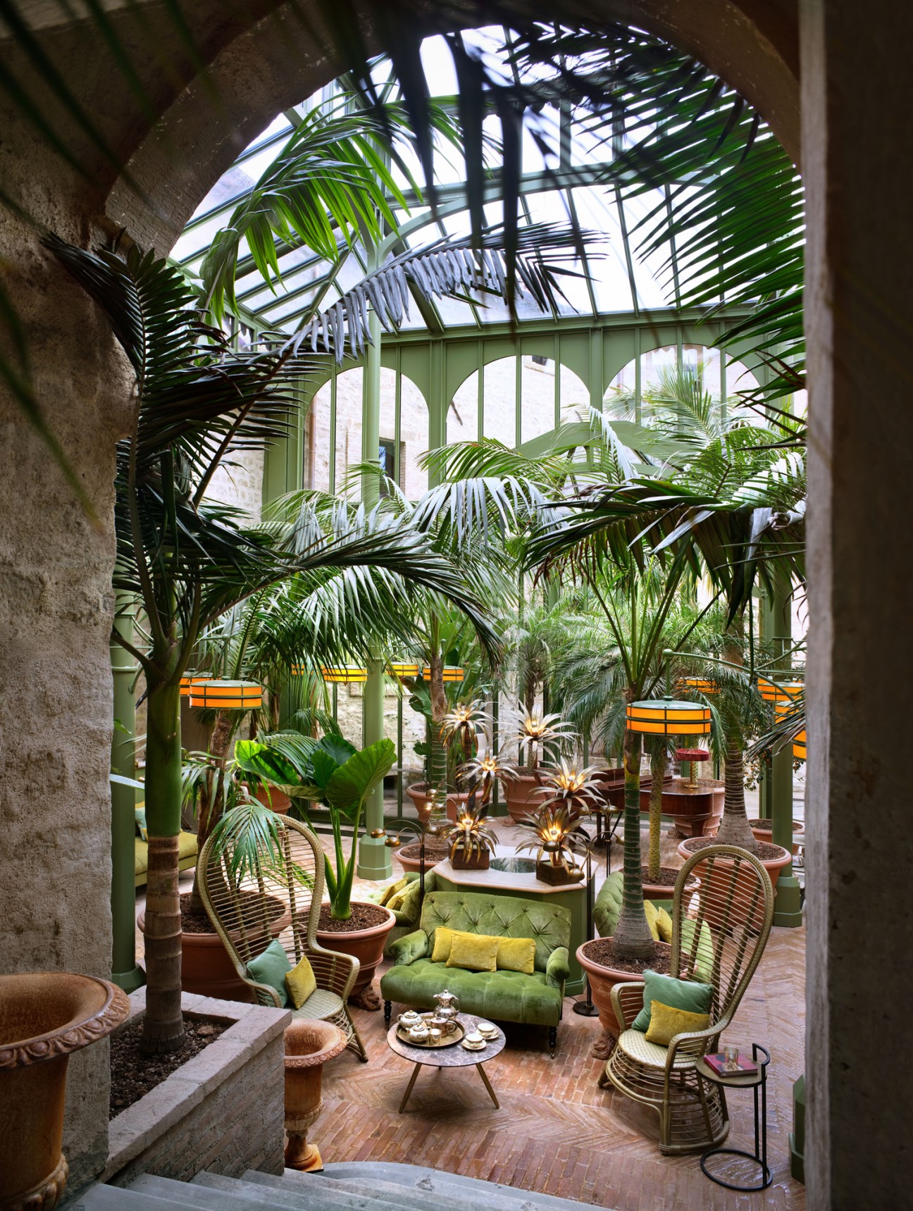 Lush tropical conservatory with palm trees, wicker furniture and glass ceiling creating an indoor garden atmosphere