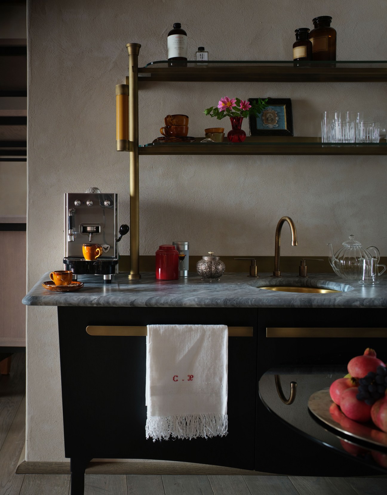 Elegant kitchen counter with espresso machine, marble countertop, brass fixtures and shelving with glassware and bottles