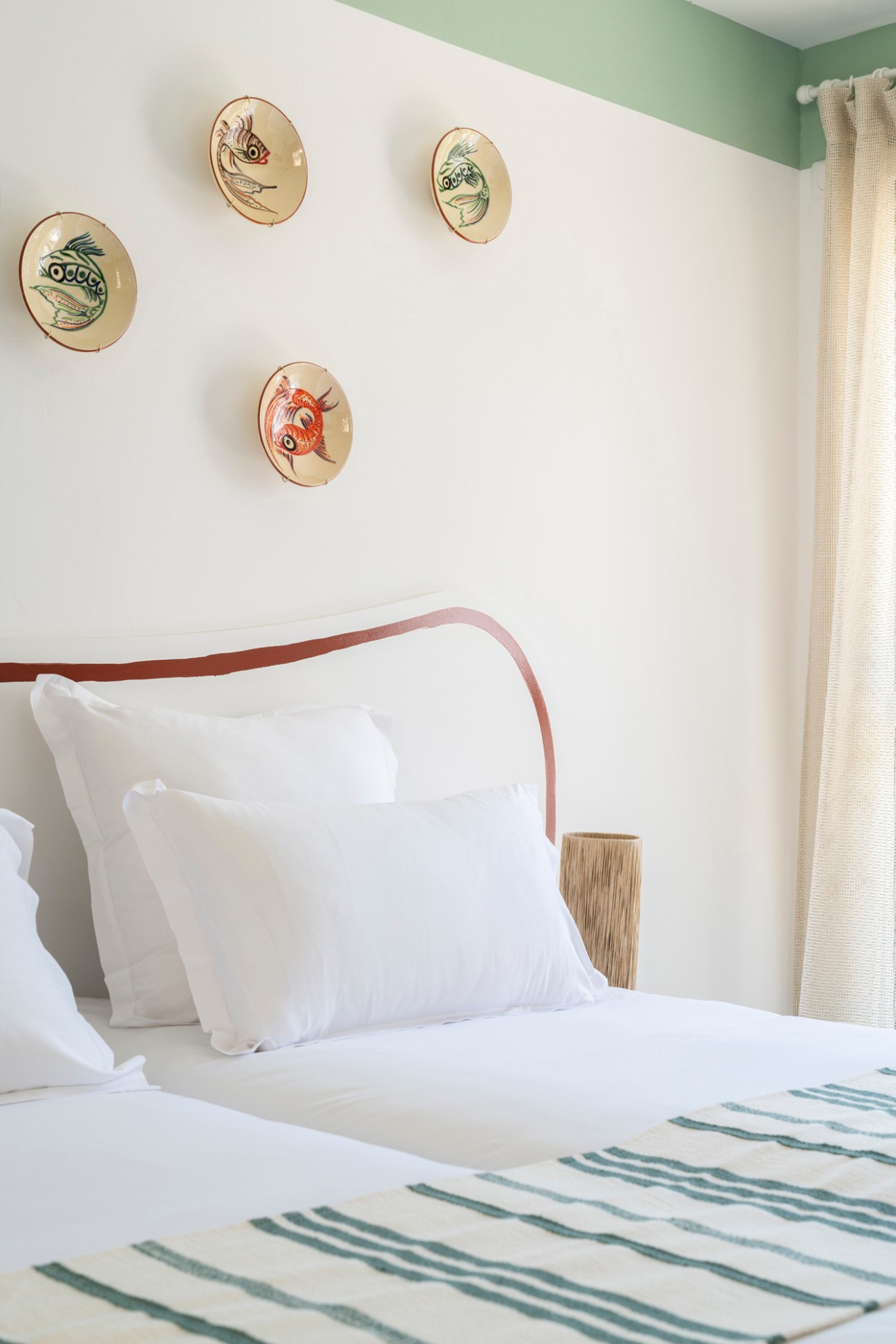 Cozy hotel bedroom with decorative fish plates on white wall above bed with striped throw