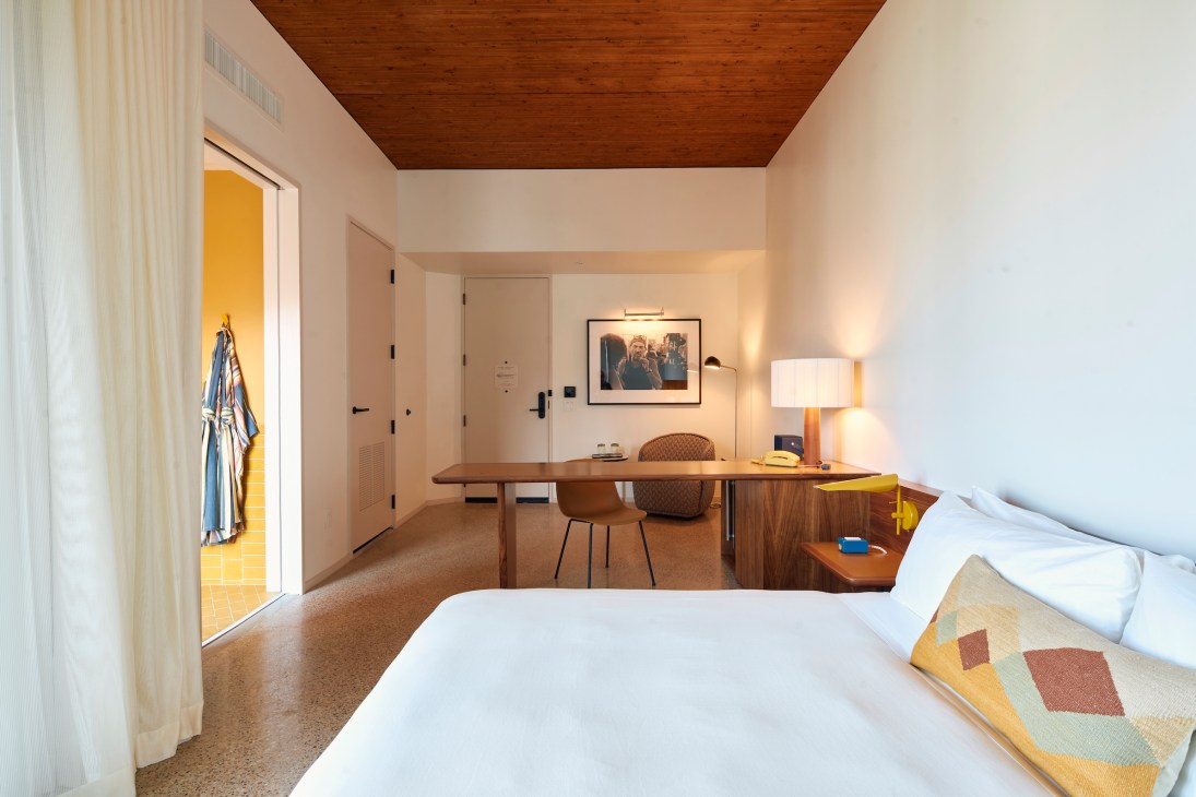 Hotel Magdalena bedroom with yellow walls, white bedding, wood ceiling, desk area and colorful throw blanket