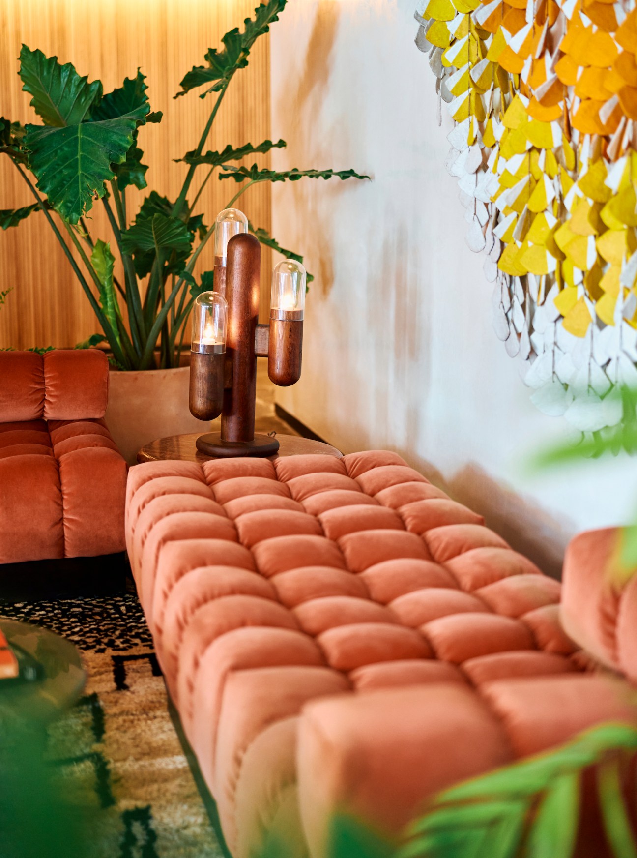 Modern lobby interior with tufted coral velvet seating, dark wood side table with sculptural lamp, and hanging plants