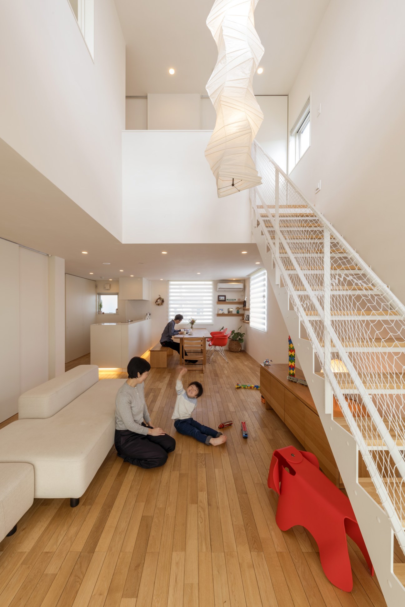 Interior of a Muji House in Nagoya with a mother and child playing in an open living space with wooden floors, white walls, and a sculptural spiral staircase.