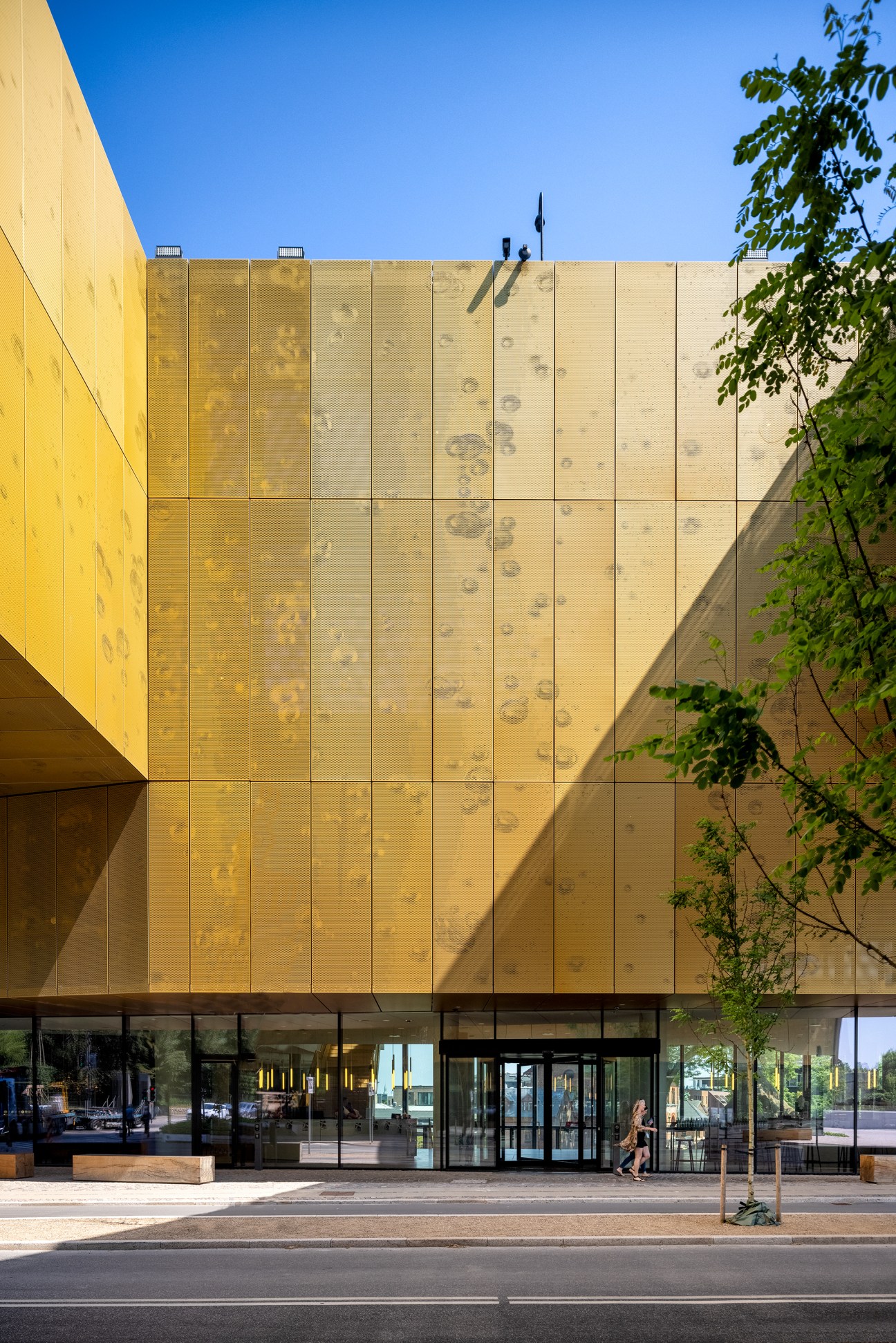 Modern glass entrance to Carlsberg headquarters with golden facade panels and person walking past