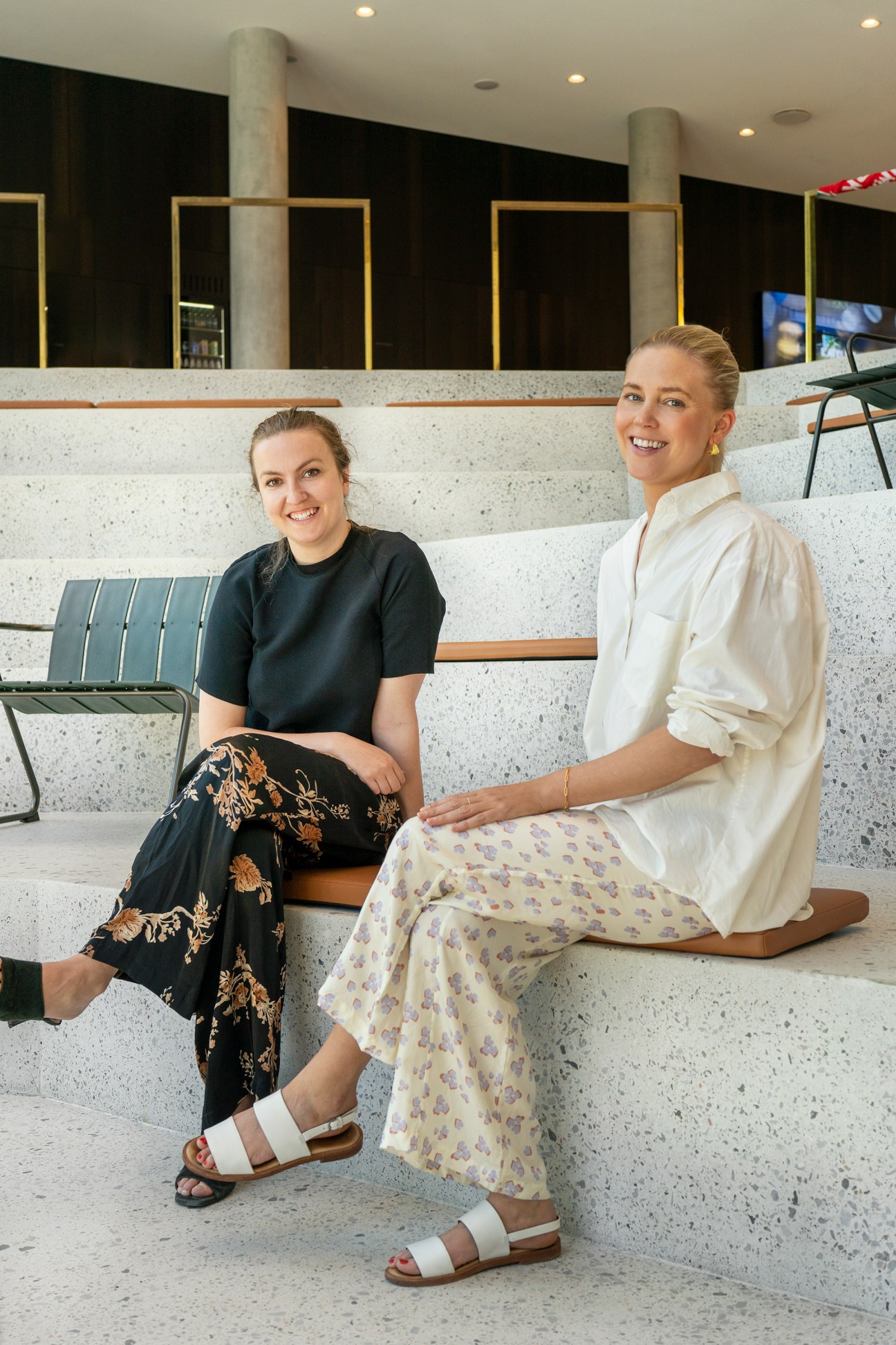 Two female Carlsberg employees Caroline Jacobsen and Nina Brønden Jakobsen sitting on concrete steps in modern office