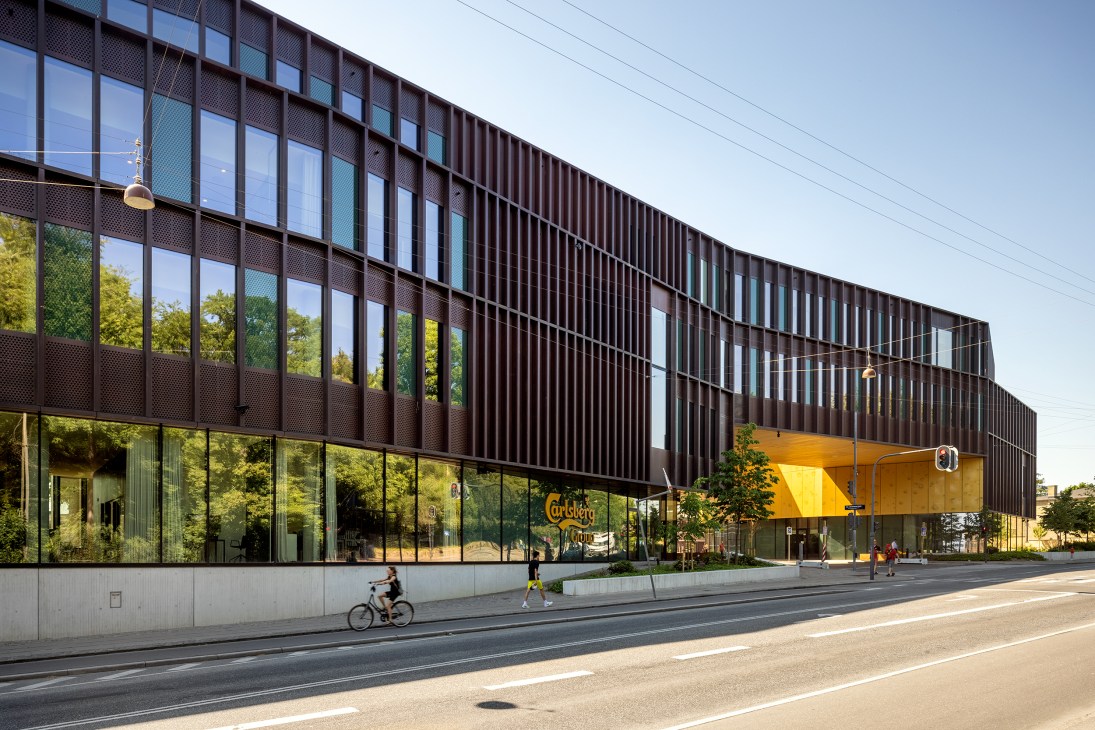 Modern Carlsberg headquarters building with dark facade and glass windows, featuring wing arching over access road