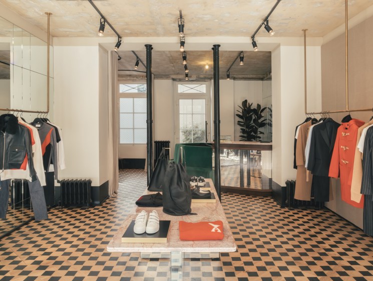 Modern Ami clothing store interior with checkerboard floor, hanging garments on both sides, and central display table