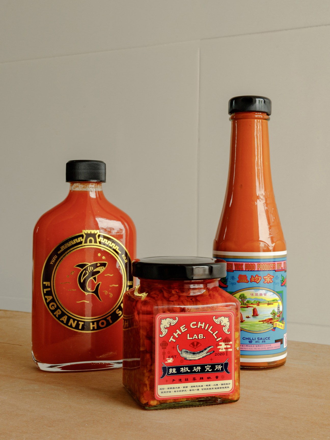Three bottles of Hong Kong hot sauce brands including Flagrant Hot Sauce and The Chilli Lab on wooden surface