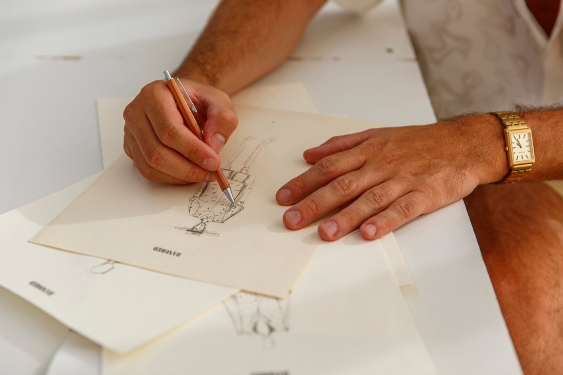 Person's hands sketching technical drawings on paper with pen, wearing gold watch