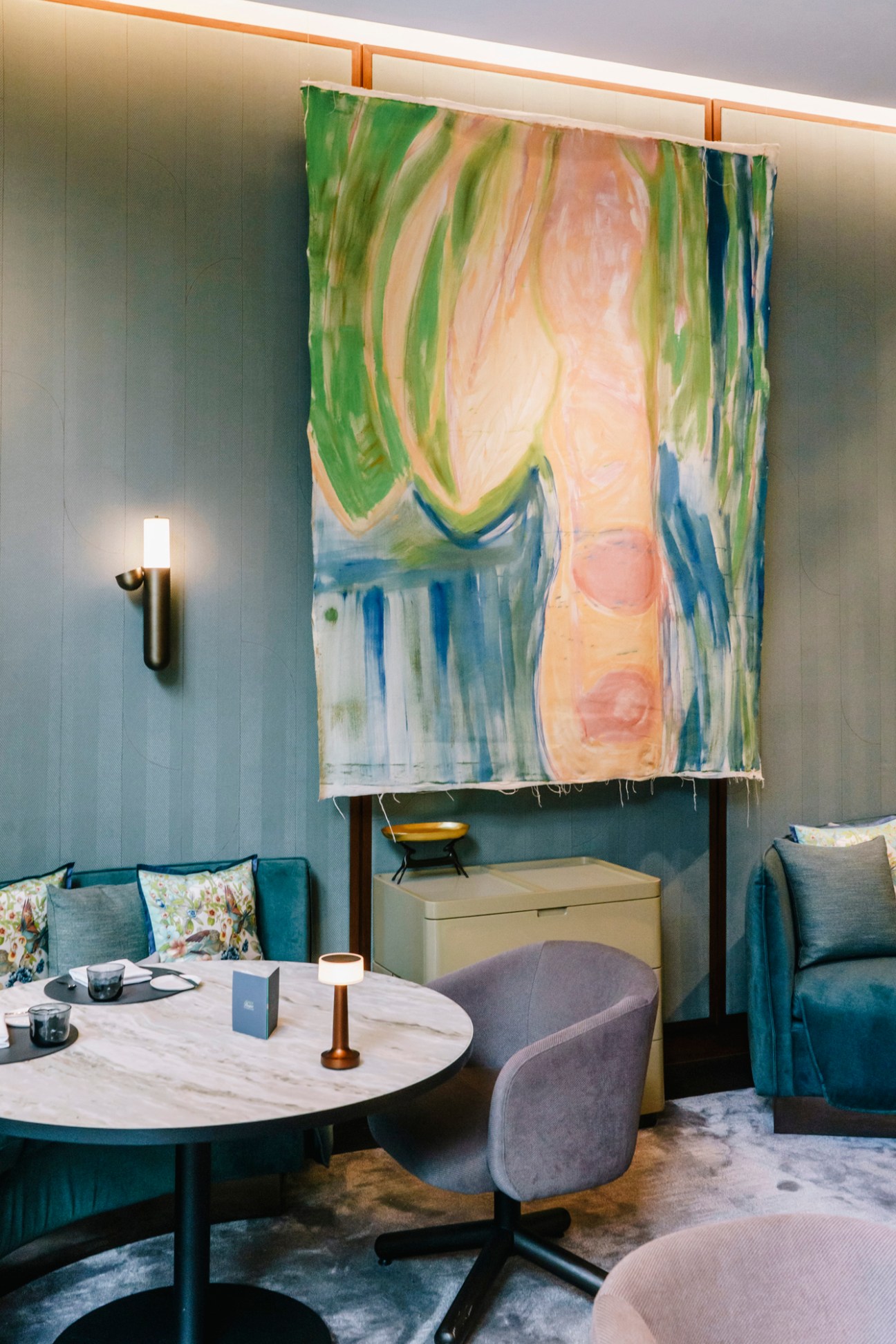 Colorful abstract artwork by Vivian Suter hanging above seating area in modern restaurant interior