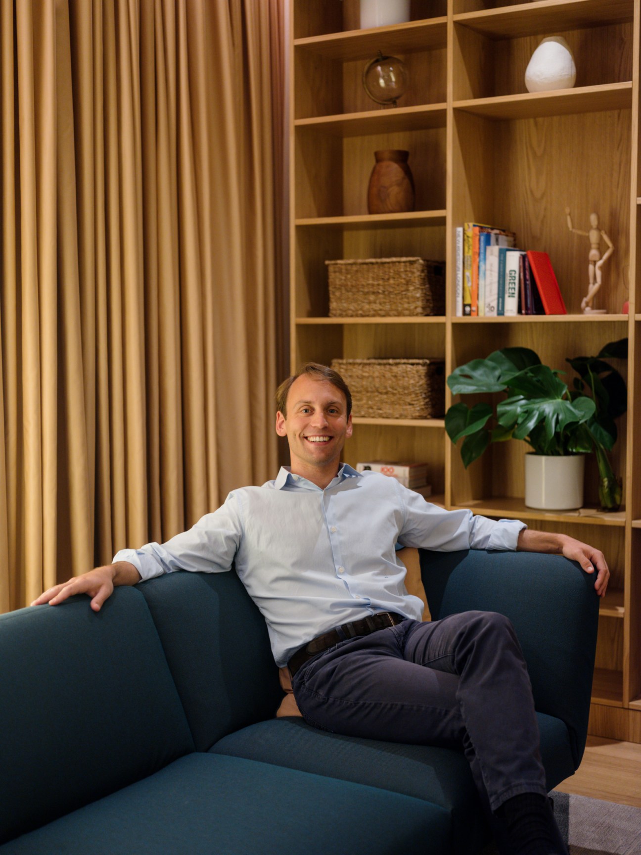 Julius Meinl VI sitting relaxed on a blue sofa in a modern office with wooden shelving