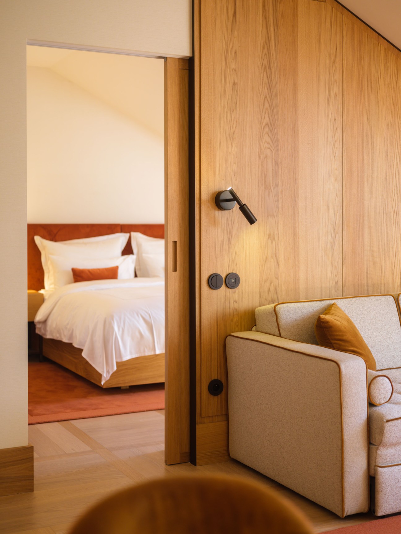 The Julius Prague hotel suite with wood-paneled walls, beige seating area and view into bedroom
