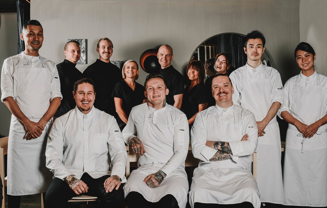 Restaurant team of chefs and staff in white uniforms and black shirts posing together in modern dining room