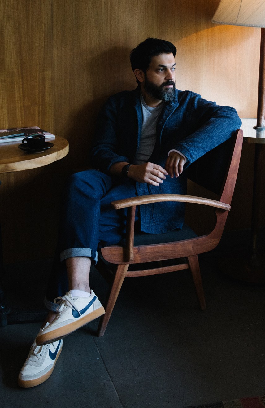 Gautam Sinha, founder of leather goods company Nappa Dori, sitting in a wooden chair in an interior setting