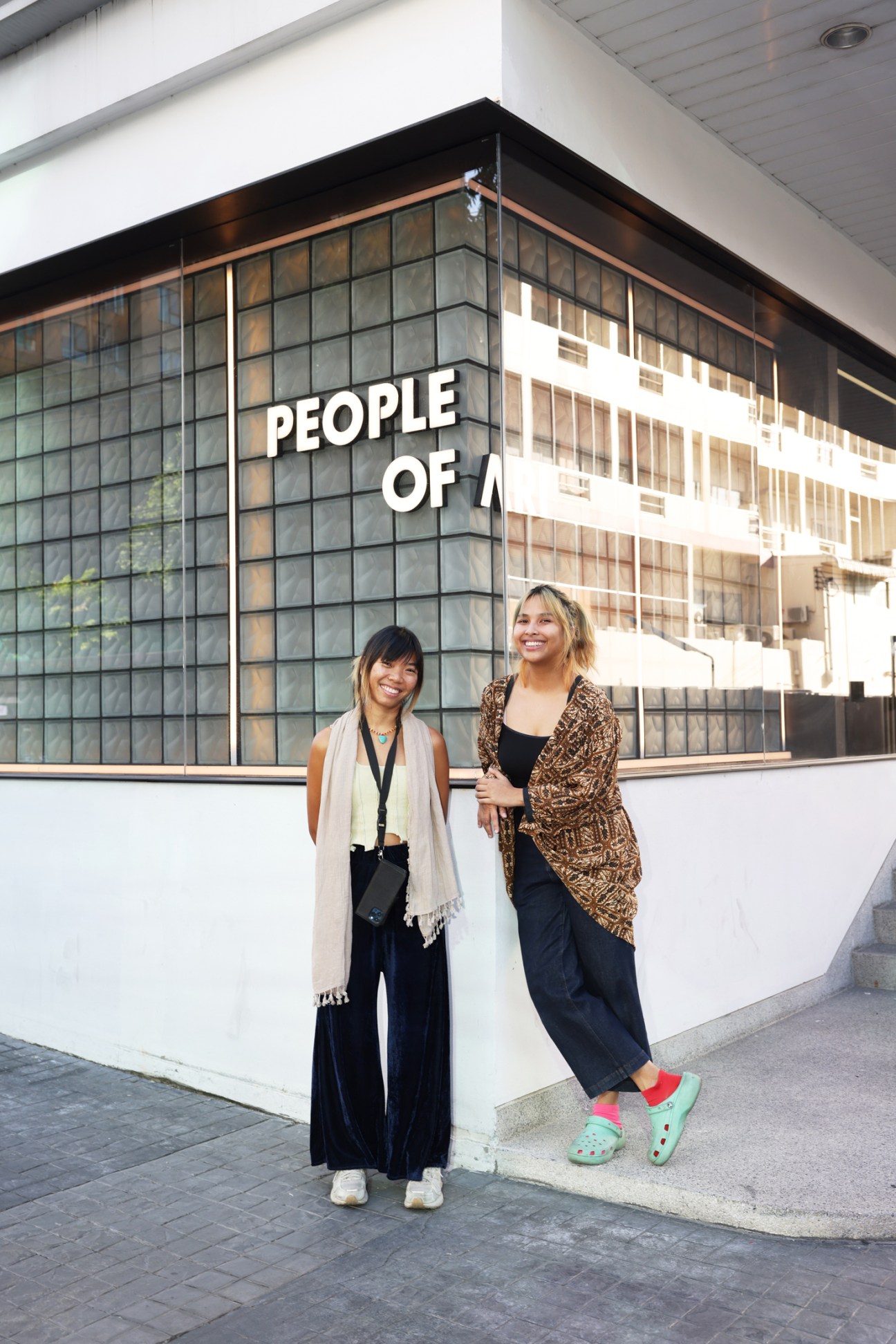 Curator Mia Tongpan standing with another person in the theatre spacestanding and smiling outside the People of Ari theatre space in Bangkok