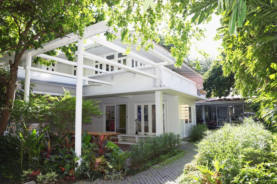 The building housing People of Ari theatre venue with modern architecture and Yellow Lane restaurant A A White modern building with upper balcony and glass doors surrounded by lush tropical plants and palm trees