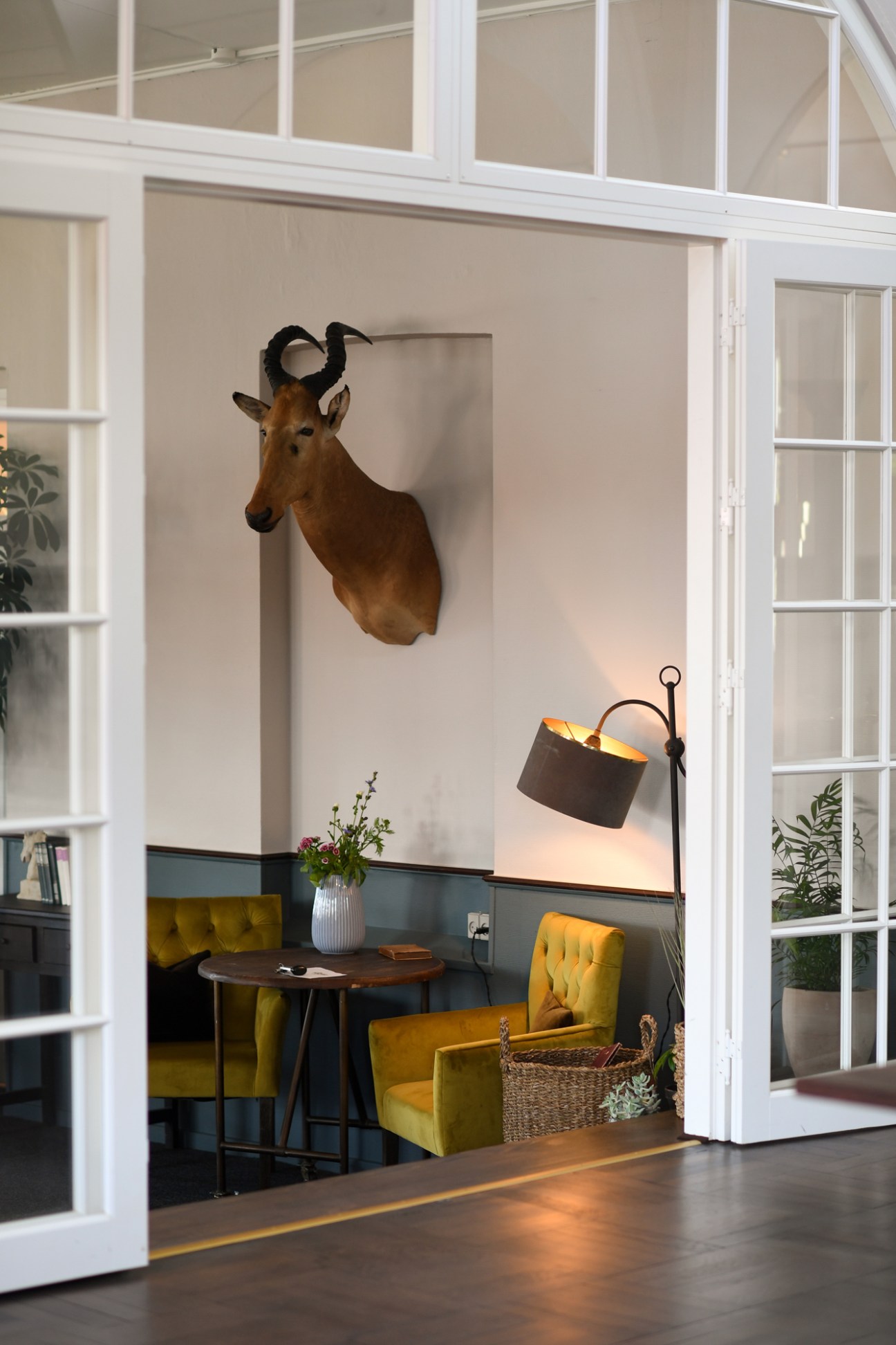 Interior lounge with mounted antelope head, yellow velvet chairs, and pendant lamp.