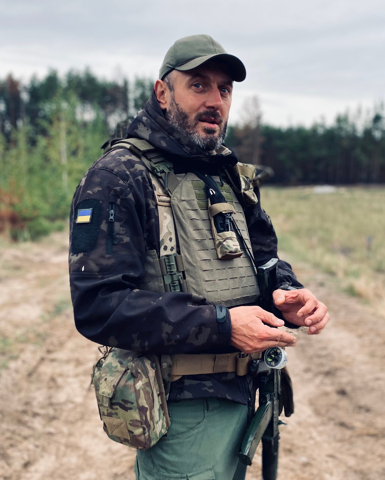 Ukrainian soldier in camouflage gear and cap standing in a forest clearing near the Belarus border.