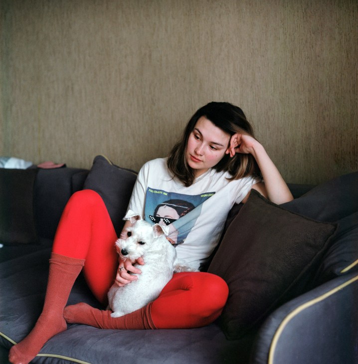 Woman in white shirt and red tights sitting on gray couch holding small white dog