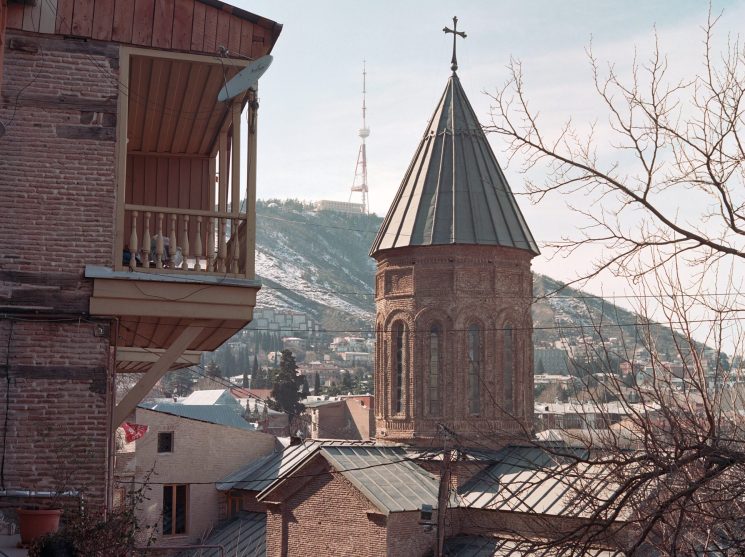 Historic church with conical tower and cross in Tbilisi's old town with traditional balconied buildings