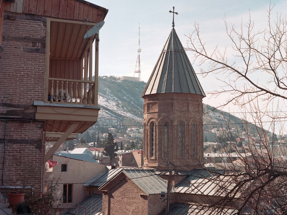 Historic church with conical tower and cross in Tbilisi's old town with traditional balconied buildings