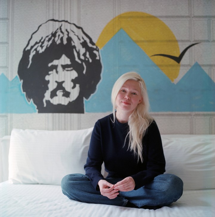 Kseniia Shabalina, a creative director who fled from Pskov to Tbilisi, sitting cross-legged on a white bed