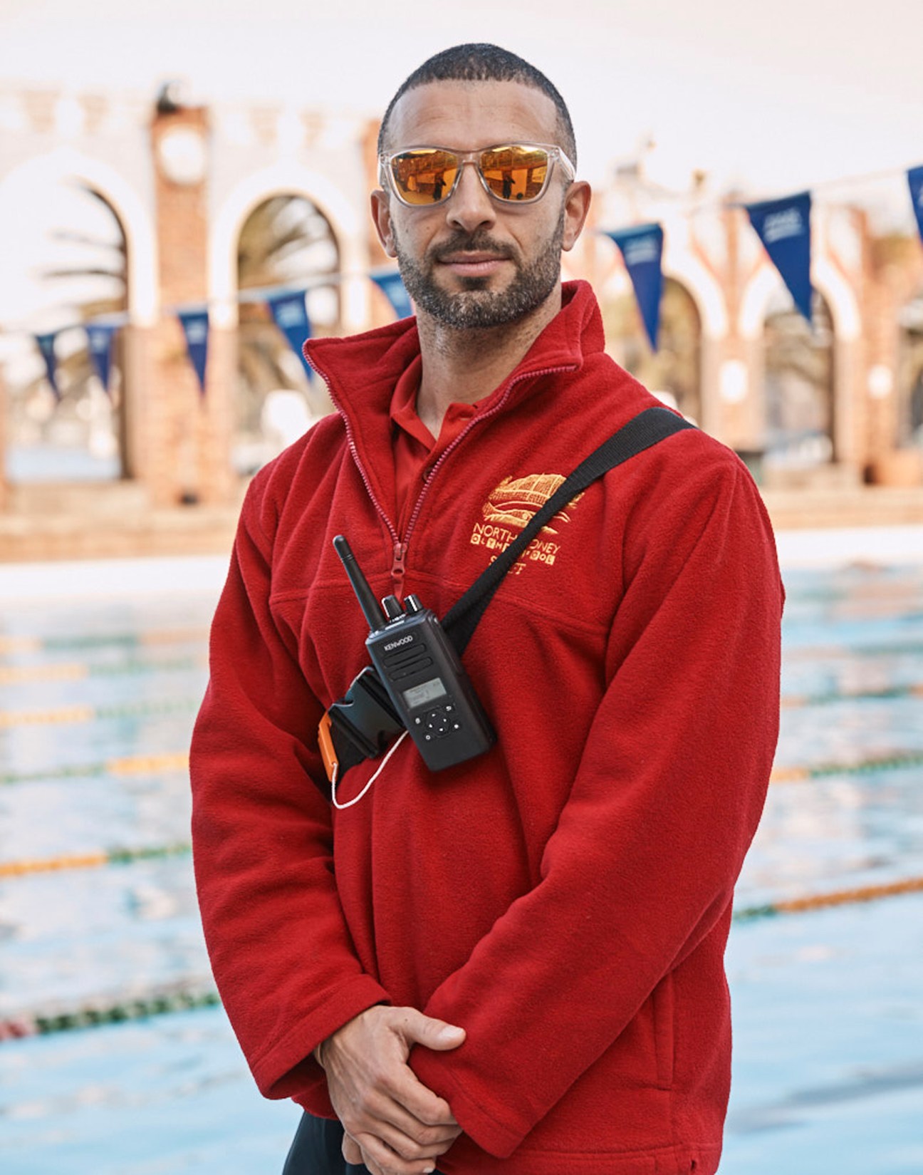 Lifeguard in red jacket with radio standing by swimming pool at North Sydney Olympic Pool