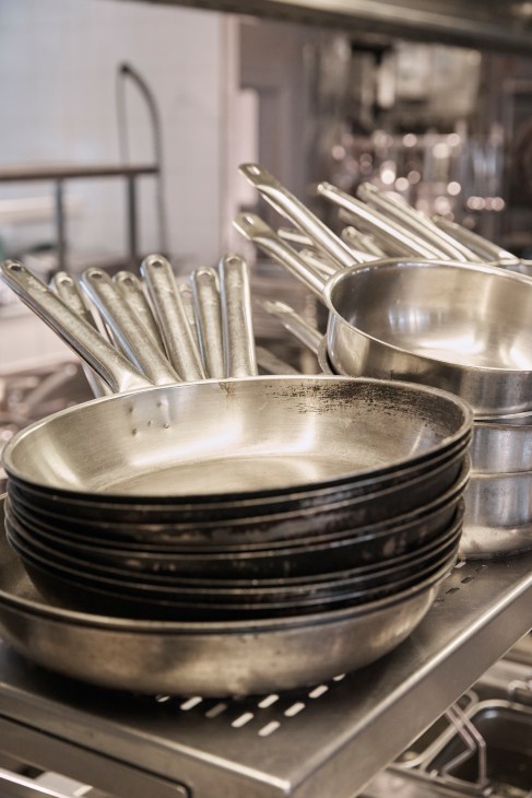 Stacked metal pans and utensils in a professional kitchen.