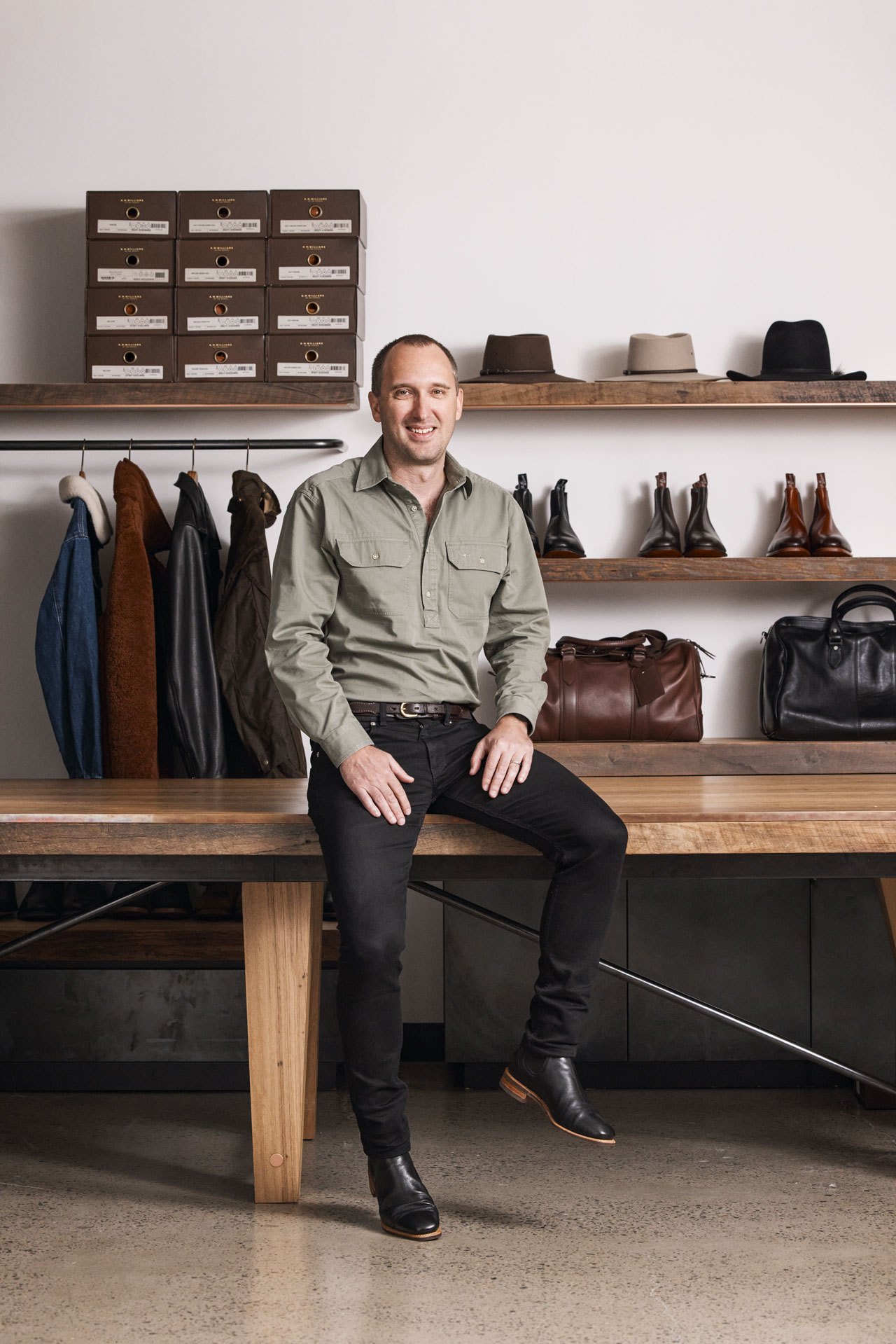 CEO Paul Grosmann sitting on wooden bench in retail store surrounded by leather goods, hats and shoe boxes