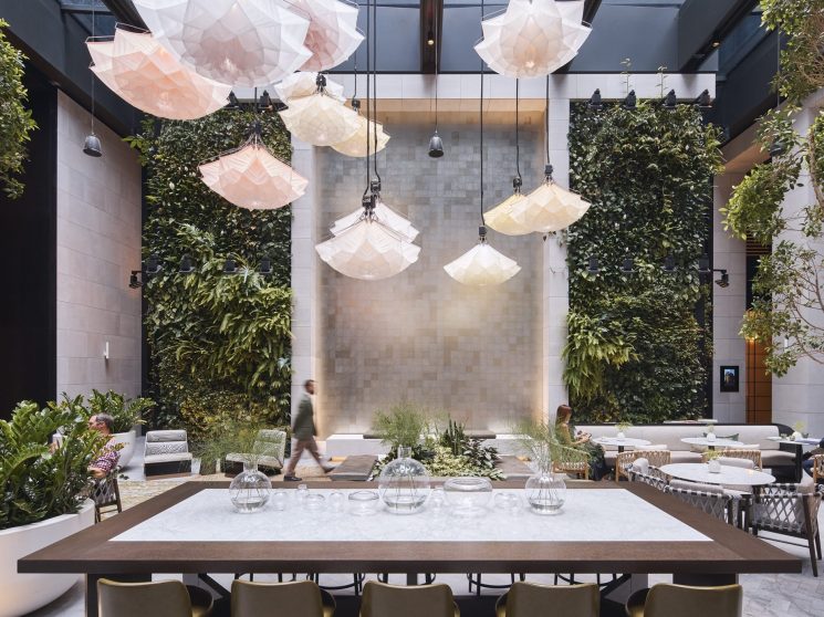 Aperture courtyard with suspended flower-like lights by Studio Drift, dining tables, and living green walls
