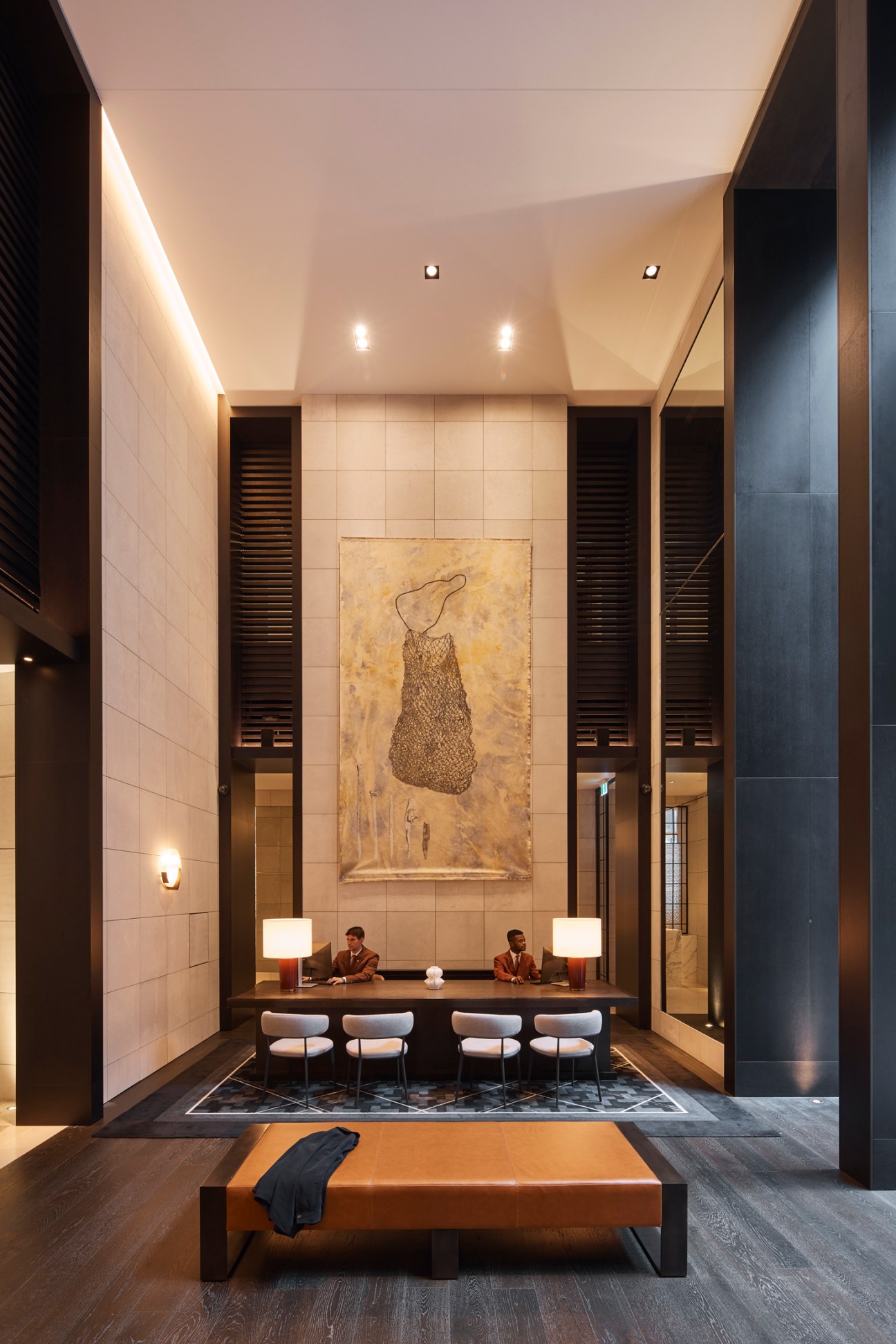 Elegant hotel reception area with high ceilings, warm lighting, leather bench seating and concierge desk
