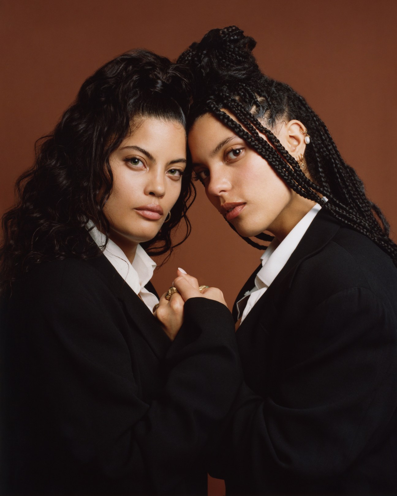 Twin sisters Lisa-Kaindé and Naomi Díaz of Ibeyi sitting together in black suits