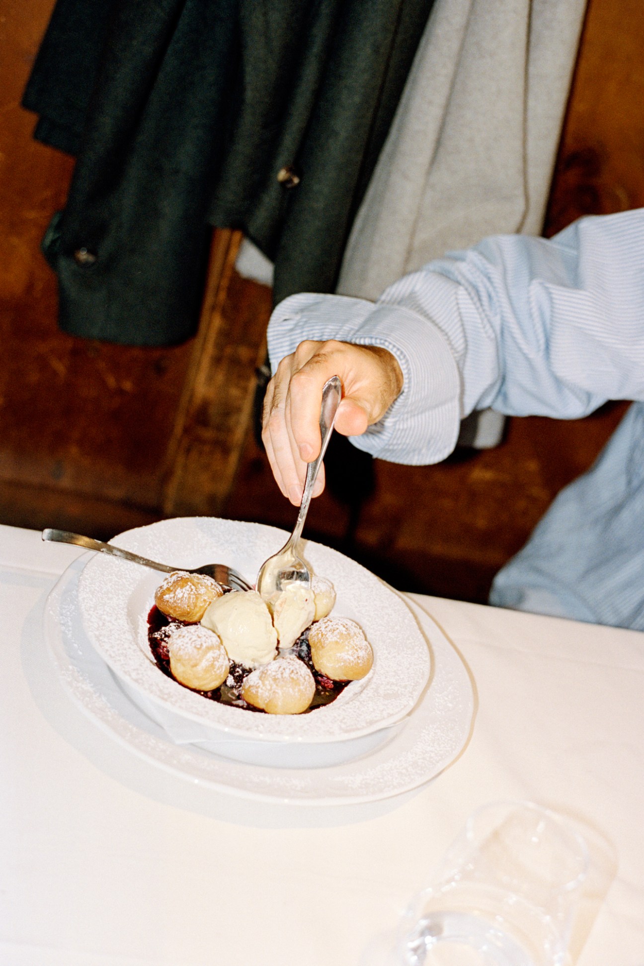 Hand pouring sauce over small round pastries dusted with powdered sugar on white plate