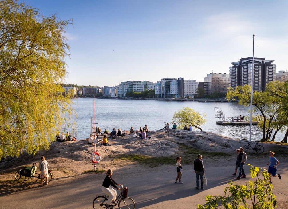 People swimming and sunbathing at an urban beach in Stockholm with city buildings visible across the water