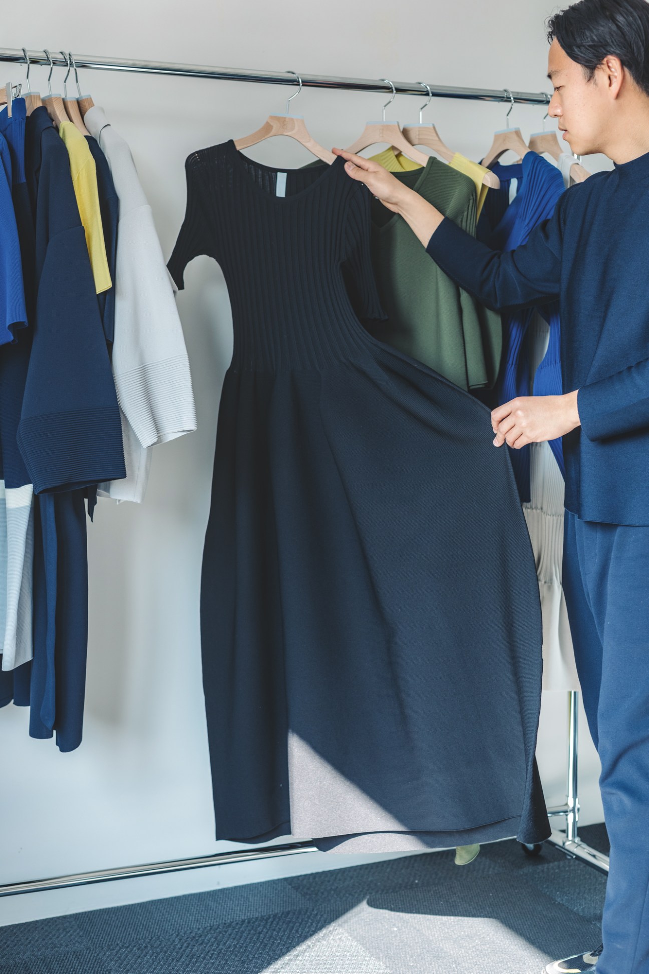Man in blue outfit examining clothes on hangers in a closet or retail space