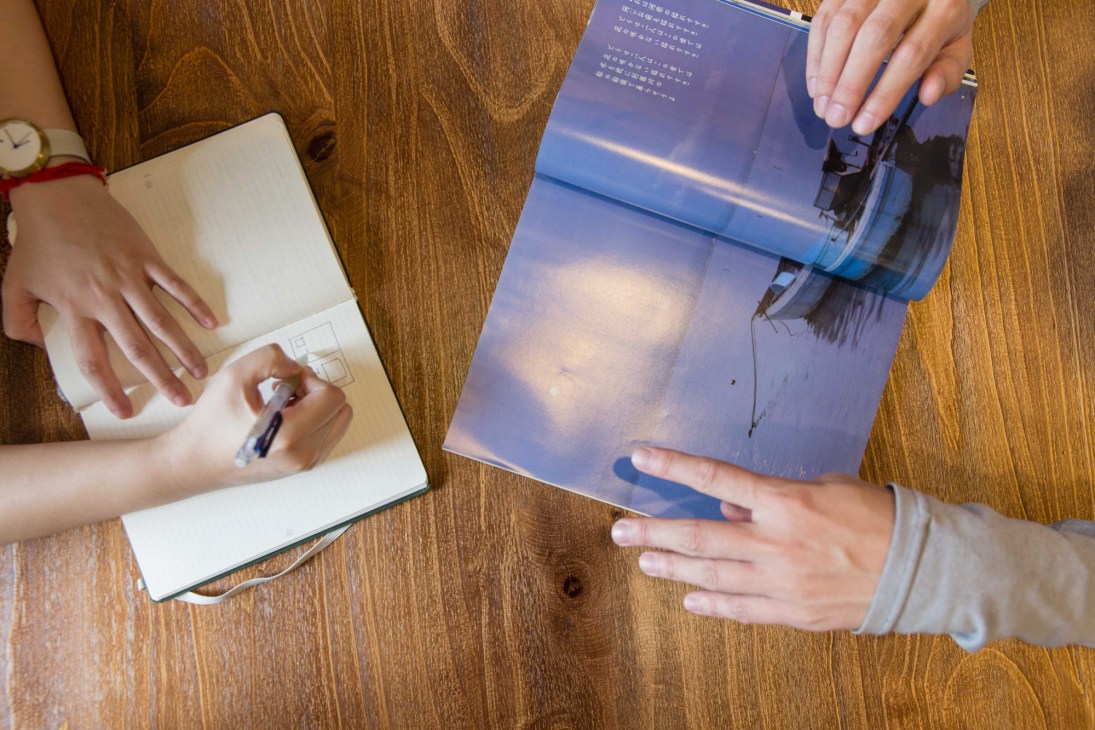 Two hands holding open QDY magazine on a wooden surface.