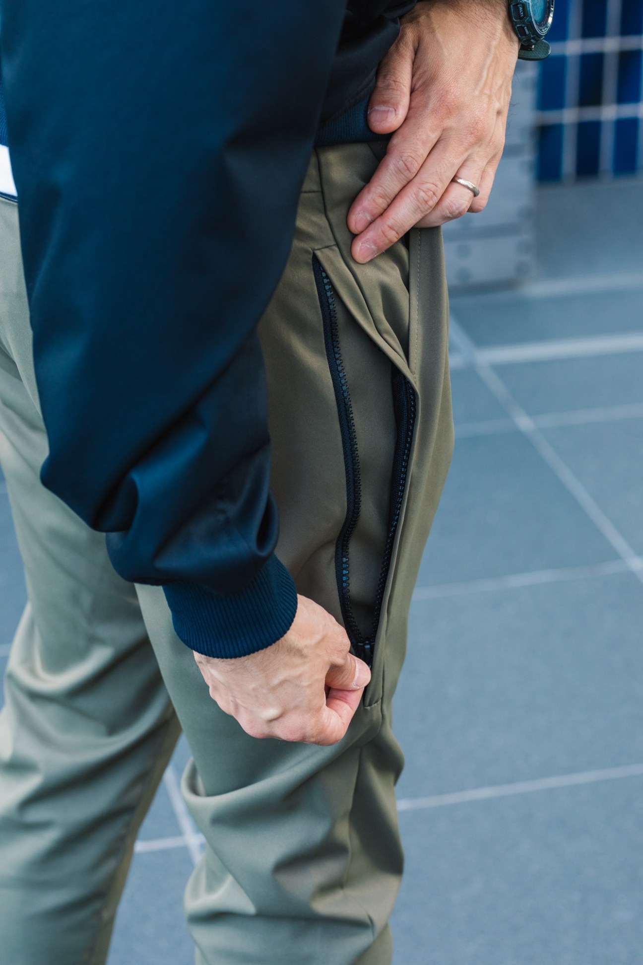 Close-up of a man's hand with a ring gripping khaki-colored work pants with a dark zipper detail.