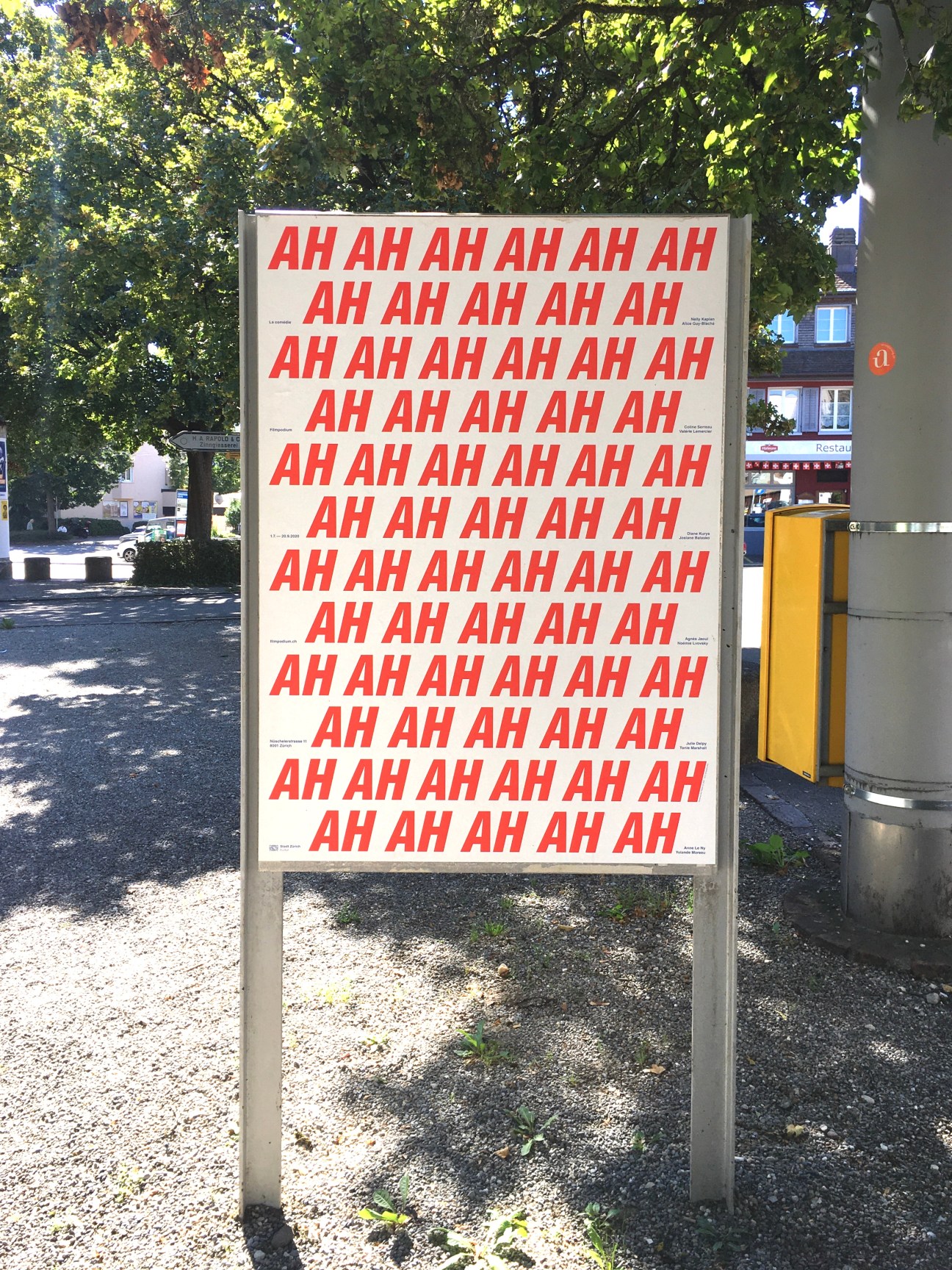 Public billboard displaying repeated red "AH" text on cream background in urban setting